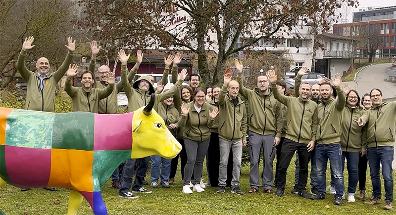 Gruppenbild der Druckwerk SH AG. 20 Personen in olivfarbenen Hoodies winken in die Kamera.